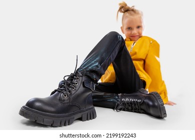 Pretty Blonde Little Girl Sitting In Studio Floor In A Leather Mustard Jacket, Black Snake Texture Leggings And Boots. High Fashion, Full Length Standing Pose, Isolated Against A Studio Background