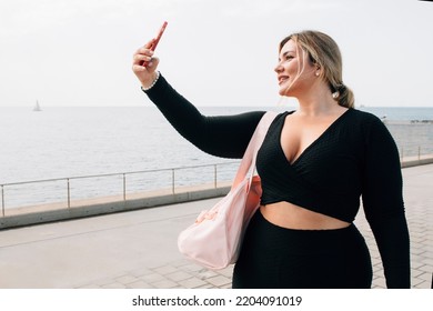 pretty blonde plus-size girl taking a selfie with her cell phone in front of the beach dressed in sportswear