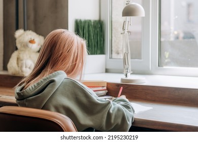 Pretty blonde teenage girl in home clothes doing homework,making notes in notebook at home at her desk,rear view.School concept. - Shutterstock ID 2195230219