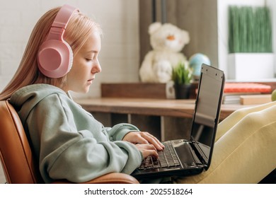 Pretty blonde teenage girl wearing headphones,using a laptop,doing homework at home.Back to school concept.School distance education at home during coronavirus pandemic,homeschooling,social media.