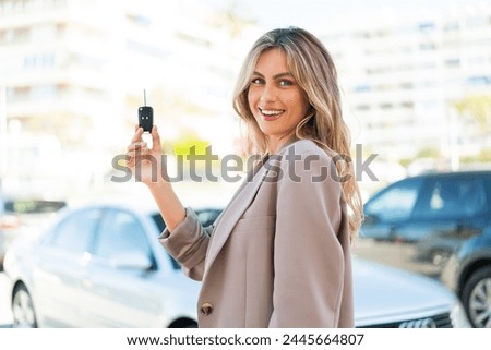 Pretty blonde Uruguayan woman holding car keys at outdoors smiling a lot