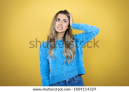 Pretty blonde woman with long hair standing over yellow background putting one hand on her head smiling like she had forgotten something