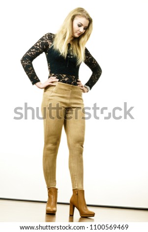 Pretty blonde woman wearing fashionable black lace top with long sleeve, brown trousers and high heels boots. Style of fashion model.