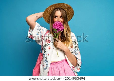 Pretty blonde woman wearing stylish colorful summer outfit having fun and holding peanut flower, studio blue background.