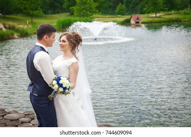 Pretty bride and groom smiling in nature near the lake with fountain