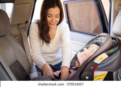 Pretty brunette fastening the seat belt of a child car seat before going for a ride with her baby