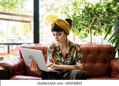 Pretty brunette girl checks her mail on small portable laptop while waiting her order in cafe shop. She travels during her summer vacations and sometimes works remotely - Shutterstock ID 645550855