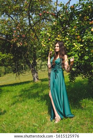 Pretty brunette girl standing near apple tree. In the garden of the fruit trees. Gorgeous girl in a silk dress. Style of the goddess.