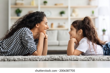 Pretty Brunette Mother And Daughter Posing At Home, Laying On Carpet In Living Room, Looking At Each Other And Smiling, Side View, Panorama. Beautiful Mom And Kid Bonding At Home, Motherhood Concept