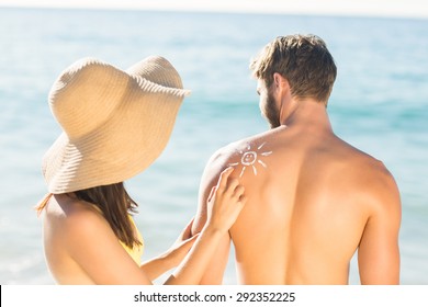 pretty brunette putting sun tan lotion on her boyfriend at the beach - Powered by Shutterstock