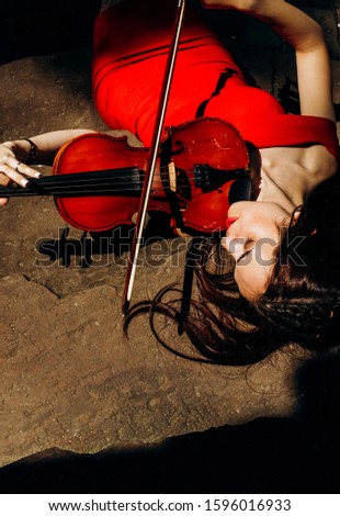 Pretty brunette in red dress holds violin in her hands