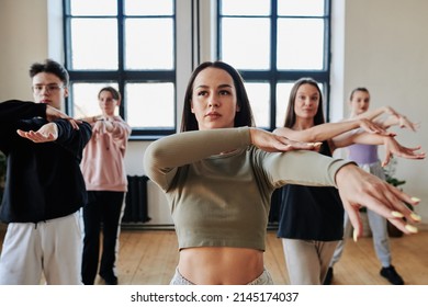 Pretty brunette teenage girl and other teens repeating new vogue dance movements after instructor or leader of performance team