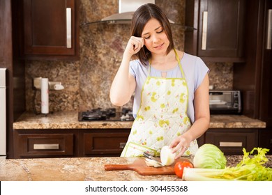 Pretty brunette wearing an apron cutting some onions in the kitchen and crying