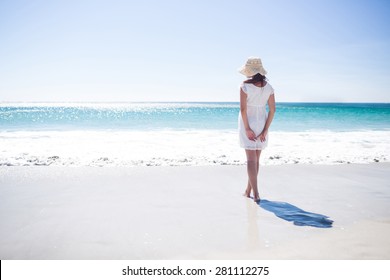 Pretty brunette wearing straw hat and walking in the water at the beach
