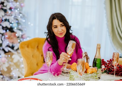 Pretty Brunette Woman With Long Hair In Bright Winter Sweater Posing With Gold Glass Of Champagne Sitting Near Christmas Table. Holiday Concept