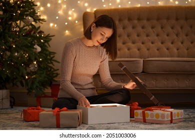 Pretty brunette woman opens an adorable present holding a white Christmas globe with lights in background - Powered by Shutterstock