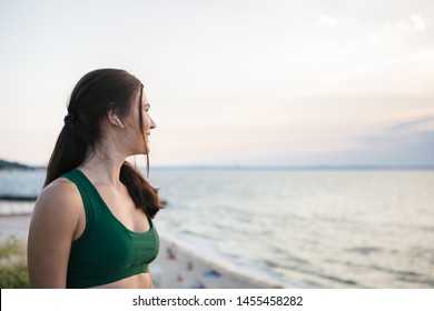 Pretty brunette woman resting after mornong jogging at the sea shore at sunrise listening to the music. - Shutterstock ID 1455458282