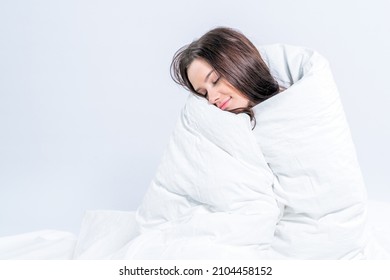 A pretty brunette, wrapped in a snow-white blanket, sits on the bed. Keep warm with a warm blanket. Laziness.