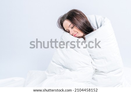 A pretty brunette, wrapped in a snow-white blanket, sits on the bed. Keep warm with a warm blanket. Laziness.