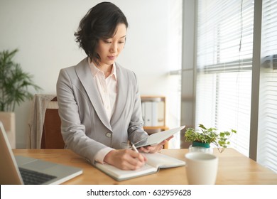 Pretty Business Lady Reading Data On Tablet Computer And Taking Notes