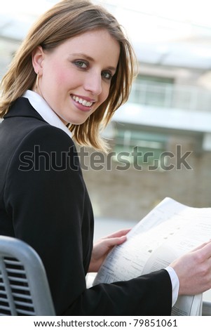 A pretty business woman reading the newspaper outside her company