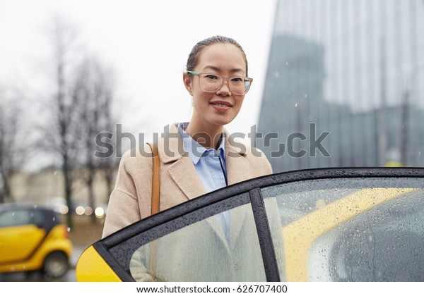 Pretty\
businesswoman looking at camera by open taxi\
door