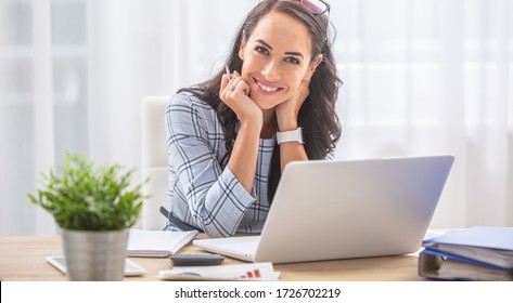 Eine hübsche Geschäftsfrau lächelt die Kamera an, während sie am Schreibtisch vor dem Computer sitzt.