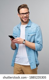 hübscher flüchtiger Mann auf blauem Jeanshemd, der sein Telefon auf grauem Hintergrund hält