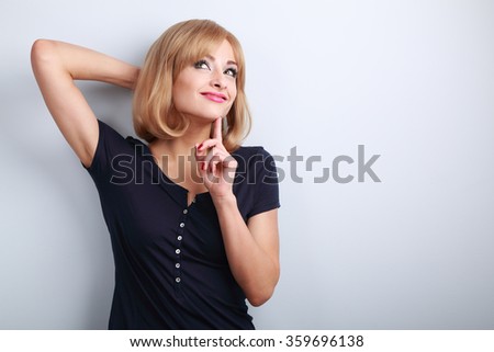 Pretty casual thinking woman with finger under face looking up on blue background