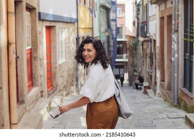 Pretty casual woman walking on a narrow European street, looking back and smiling