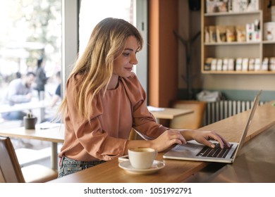 Pretty Caucasian Blonde Woman Working On Her Computer At Coffee Shop.