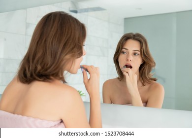 Pretty caucasian female character looking in mirror and carefully brushing teeth. Serious beautiful woman with body covered bath towel. Bathroom interior. Dental hygiene. Daily morning regimen - Shutterstock ID 1523708444