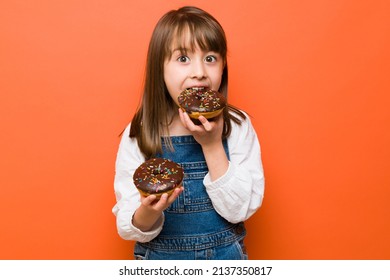 Pretty Caucasian little girl eating so much sweet food and about to get some sugar rush from so many donuts - Shutterstock ID 2137350817