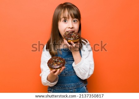 Pretty Caucasian little girl eating so much sweet food and about to get some sugar rush from so many donuts