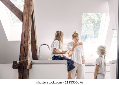 Pretty Caucasian smiling woman enjoying morning meal in kitchen with her cute daughters.