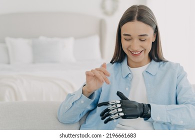 Pretty Caucasian Woman With Artificial Arm In Bedroom. Happy Girl Is Setting Her Electronic Bionic Limb. Smiling Woman Has Modern Cyber Prosthesis. Engineering And Technology Concept.