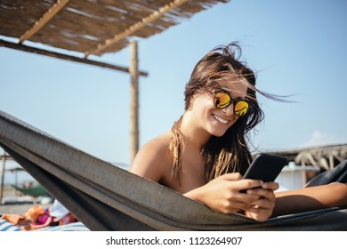 Pretty Caucasian woman lying on beach and typing on her cell phone. - Powered by Shutterstock