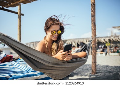 Pretty Caucasian woman lying on beach and typing on her cell phone. - Powered by Shutterstock