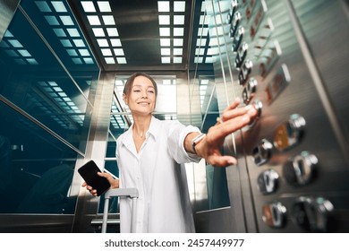 Pretty caucasian woman with suitcase and smartphone pressing button in elevator - Powered by Shutterstock