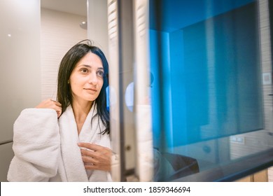 Pretty caucasian woman in white robe smillng and looking proudly to herself in a mirror - Shutterstock ID 1859346694