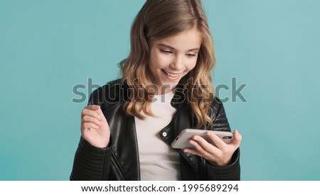 Pretty cheerful blond teenager girl watching funny videos on phone isolated on colorful background