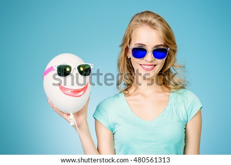 Pretty cheerful young woman in summer clothes posing with a balloon and sunglasses. 