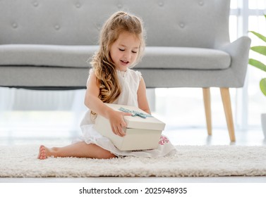 Pretty child girl with gift box at home indoors. Little female person with surprise sitting on the floor