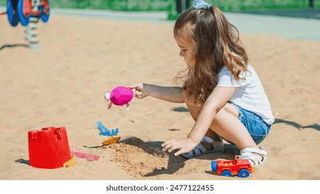 Pretty child girl playing in sand on outdoor playground. Beautiful baby in jeans shorts having fun on sunny warm summer day. Child with colorful sand toys. Healthy active baby outdoors plays games - Powered by Shutterstock