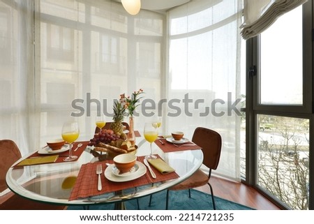 Pretty circular clear glass dining table with beveled edge surrounded by a bay window with fabric blinds