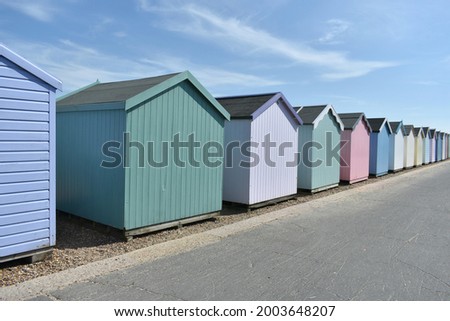 Pretty coloured beach huts lining the road side at an English seaside town on the promenade.  Wooden huts painted in pastel shades outside in summer time