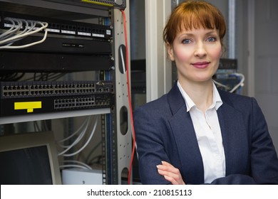 Pretty computer technician smiling at camera beside server in large data center