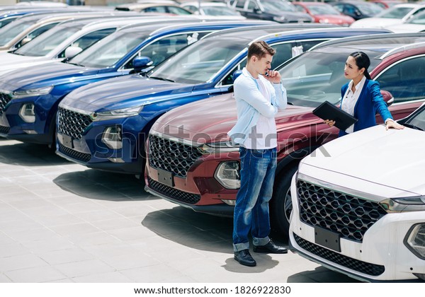 Pretty confident saleswoman showing car to\
pensive doubting young\
customer