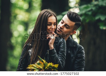 Pretty couple hugging and flirting in an urban park, woman holds a bunch of autumn leaves and listen to her man.