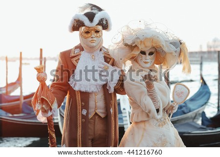 Pretty couple in rich white and golden carnival costumes poses on the berth in the dawn lights